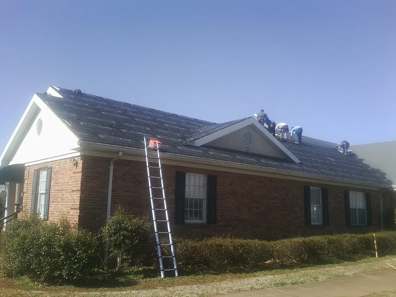 Crew tearing shingles off a brick ranch roof with a ladder set — Emergency Roof Repair work by our crew in Tiller