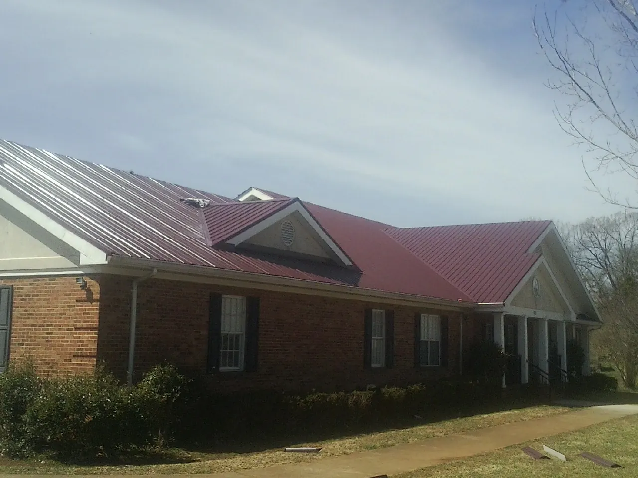 Red metal roof with gabled entries on a long brick building, from a Hail Damage Roof Repair job in Tiller