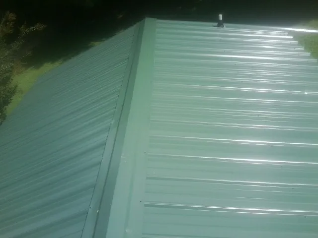 New green metal panels meeting at the ridge of a roof — Flat Roof Repair work by our crew in Tiller