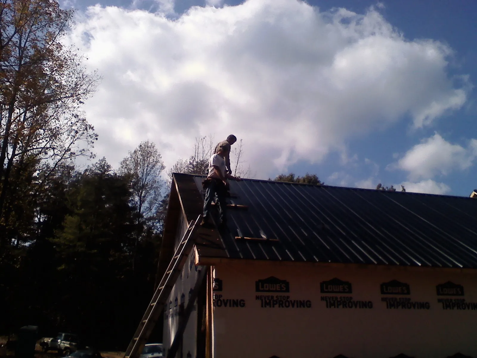 Roofer fastening dark metal panels high against a cloudy sky, from a Roof Inspection job in Tiller